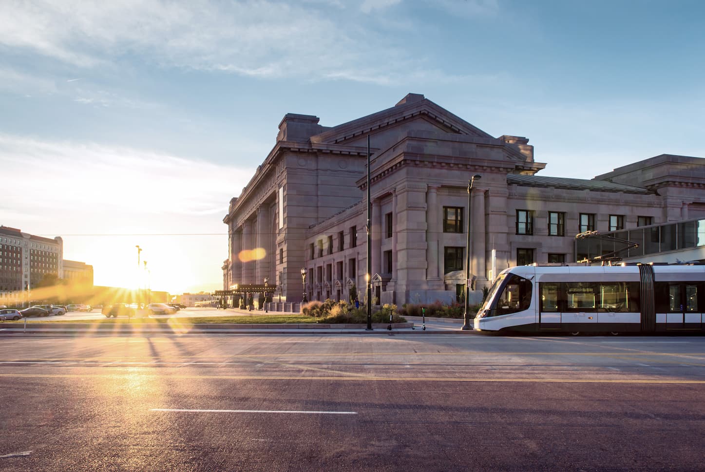 KC streetcar passing Union Station at sunset, with sunlight flaring across a wide city street.