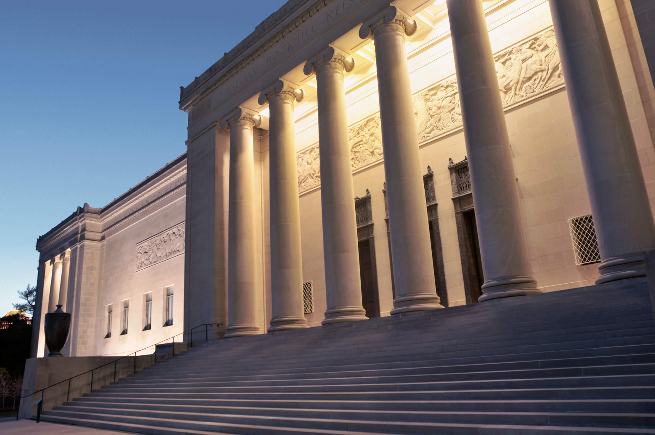 Exterior of the Nelson-Atkins Museum of Art in Kansas City, showing tall classical columns and wide stone steps illuminated at dusk.